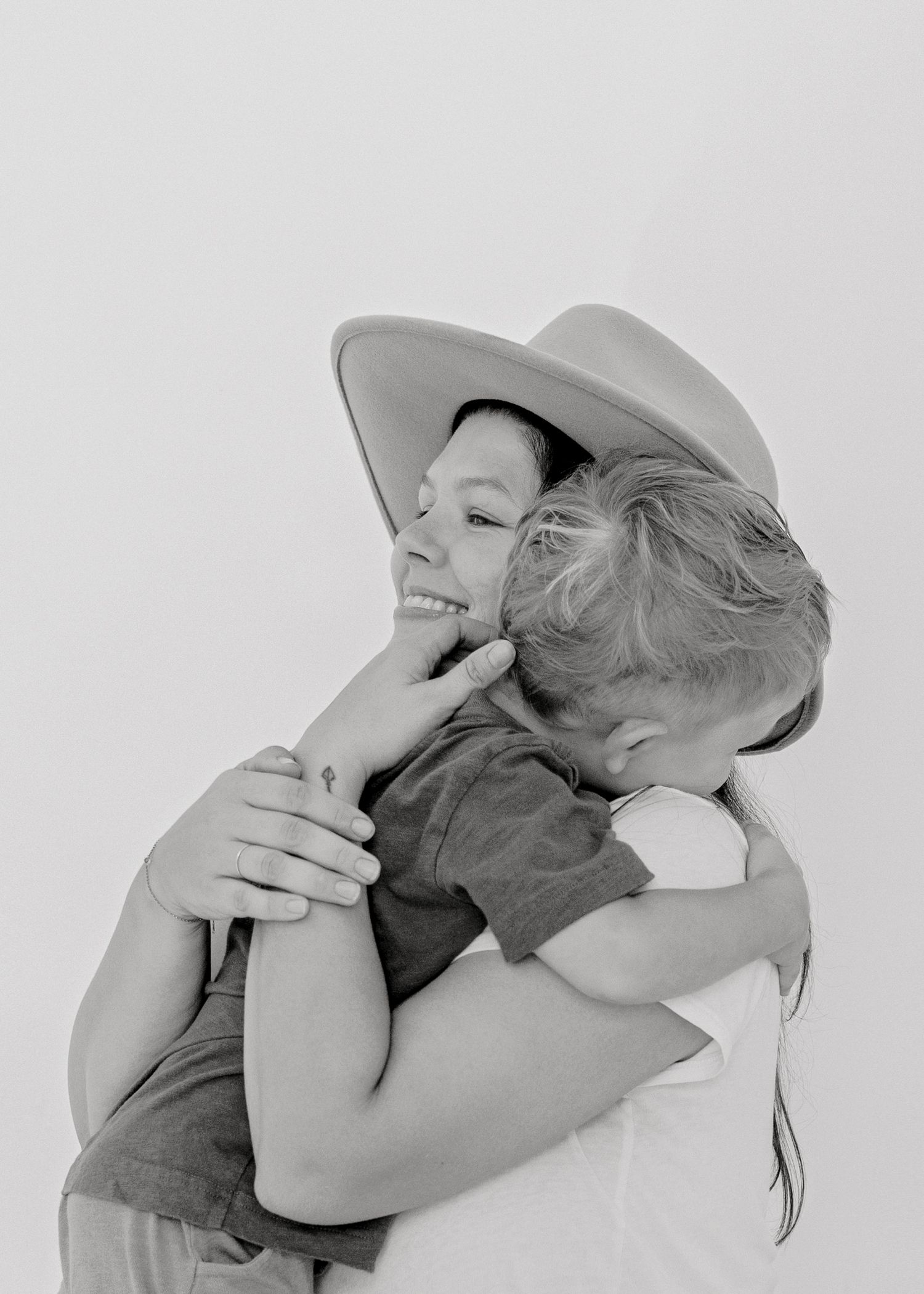 Black and white portrait of a tender embrace wearing a wide-brimmed hat against a light background.