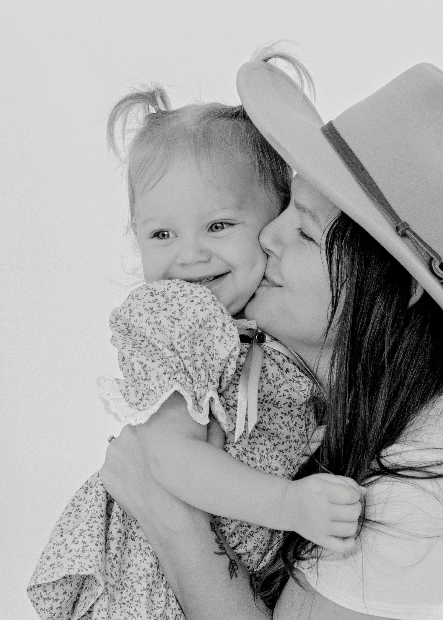 A tender black and white portrait of a sweet moment between parent and child wearing a floral dress.