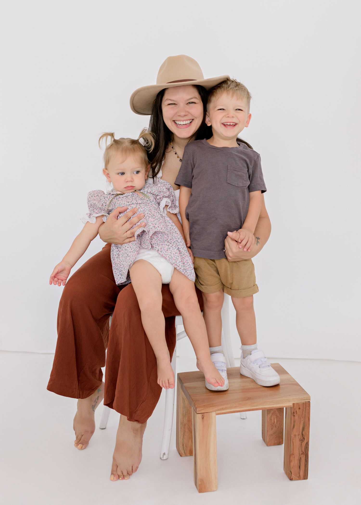A heartwarming family portrait features joyful expressions as they pose together on a wooden stool against a white backdrop.