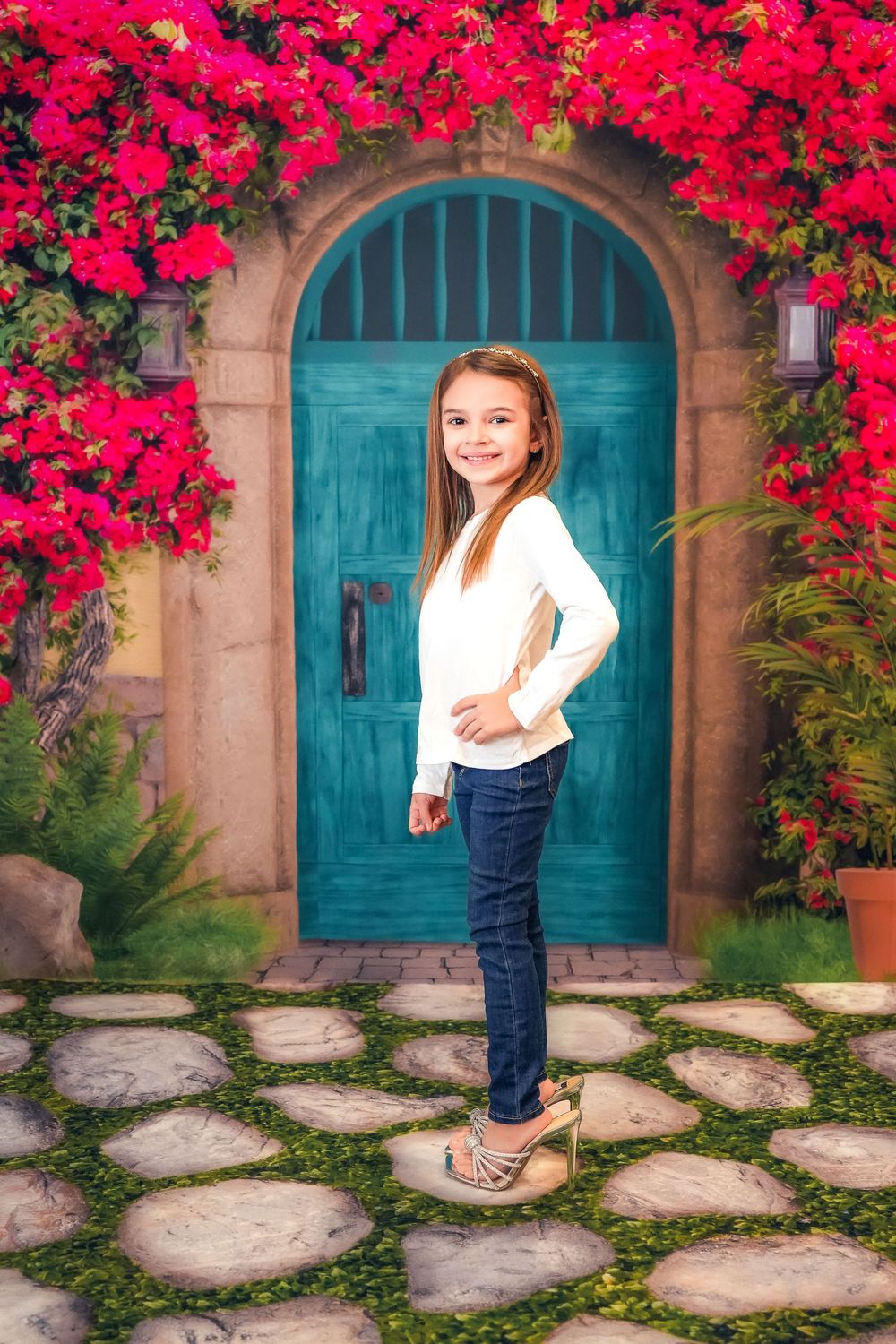 A bright turquoise arched door surrounded by vibrant pink bougainvillea flowers with stone pavers leading to the entrance.