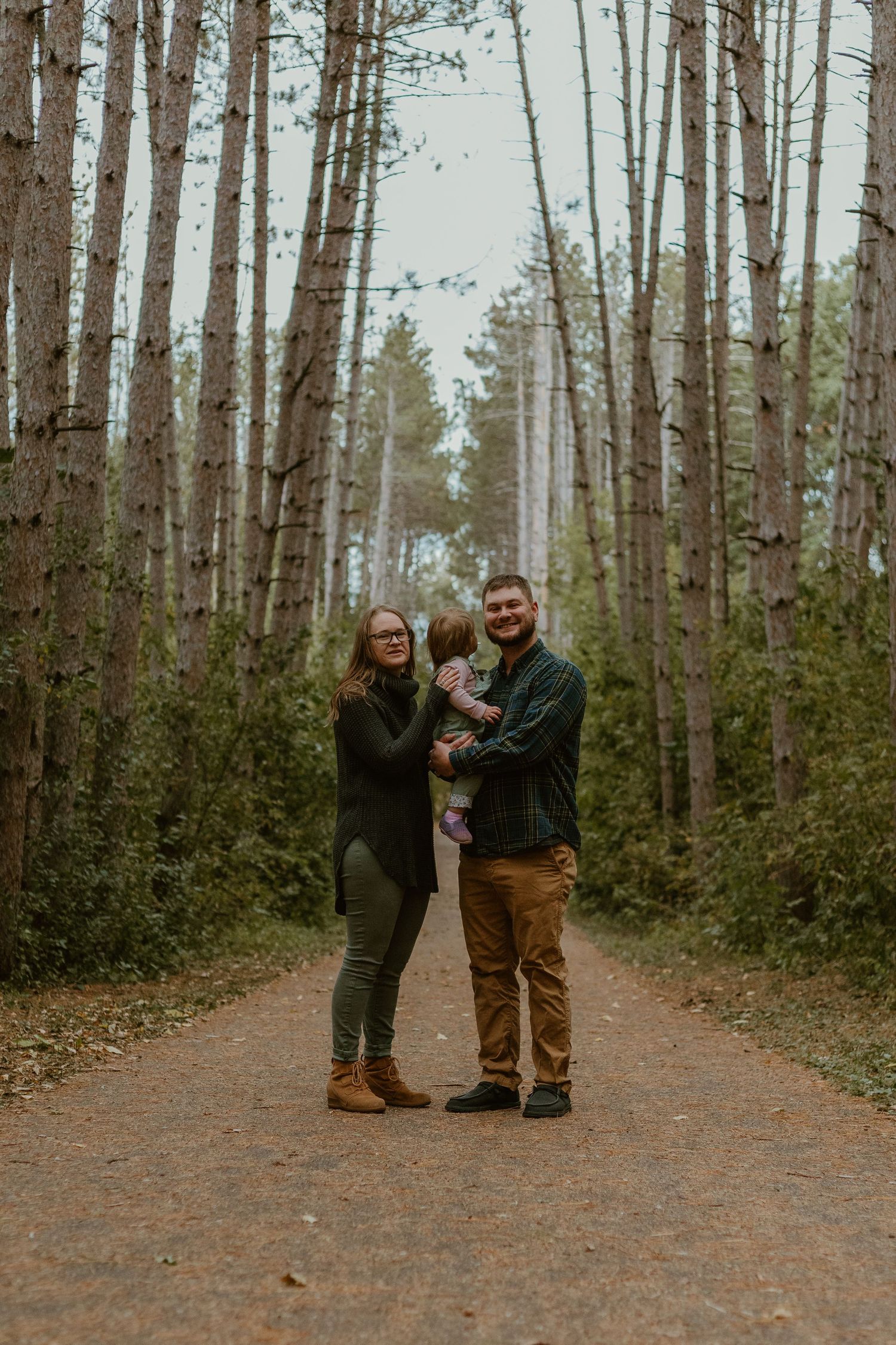 A couple stands together on a dirt path surrounded by tall birch trees in a peaceful forest setting.