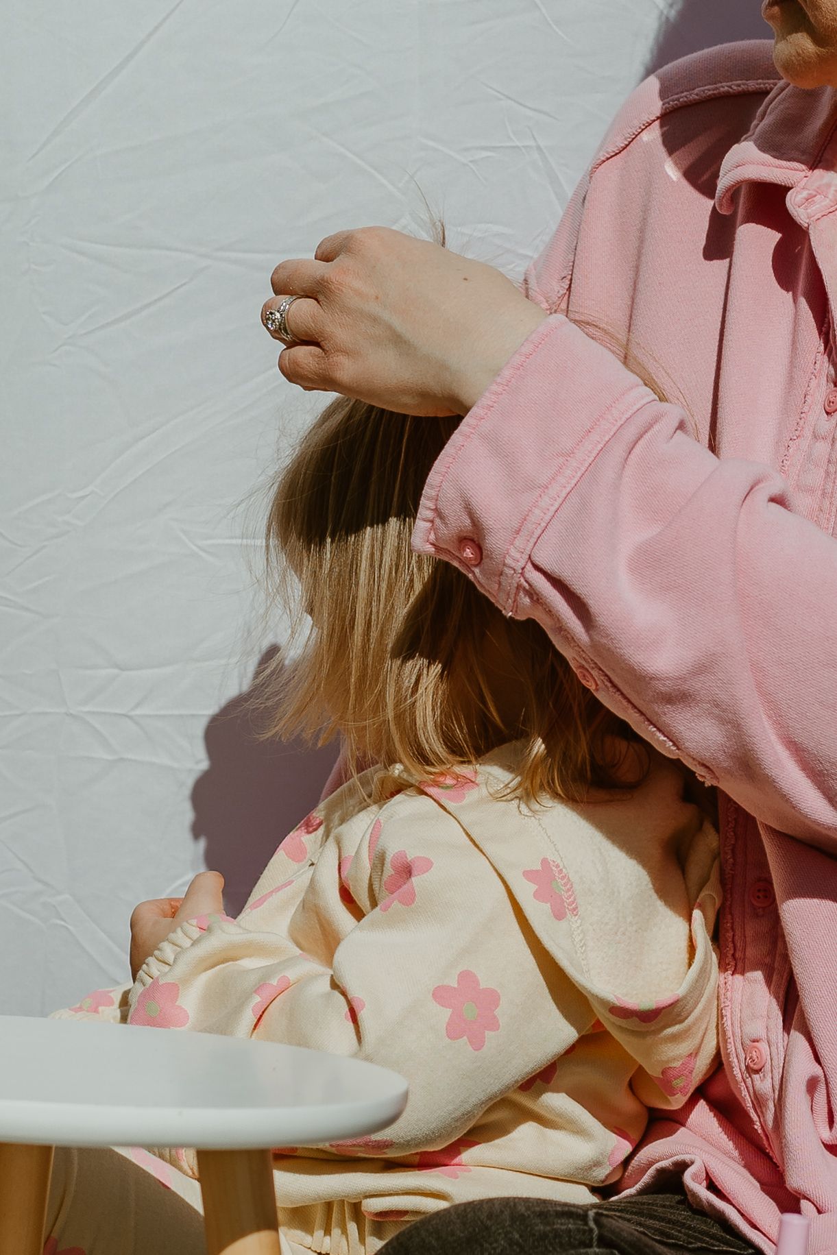 A person in a pink sweater sits cross-legged on a white backdrop with tulips and a small wooden stool nearby.