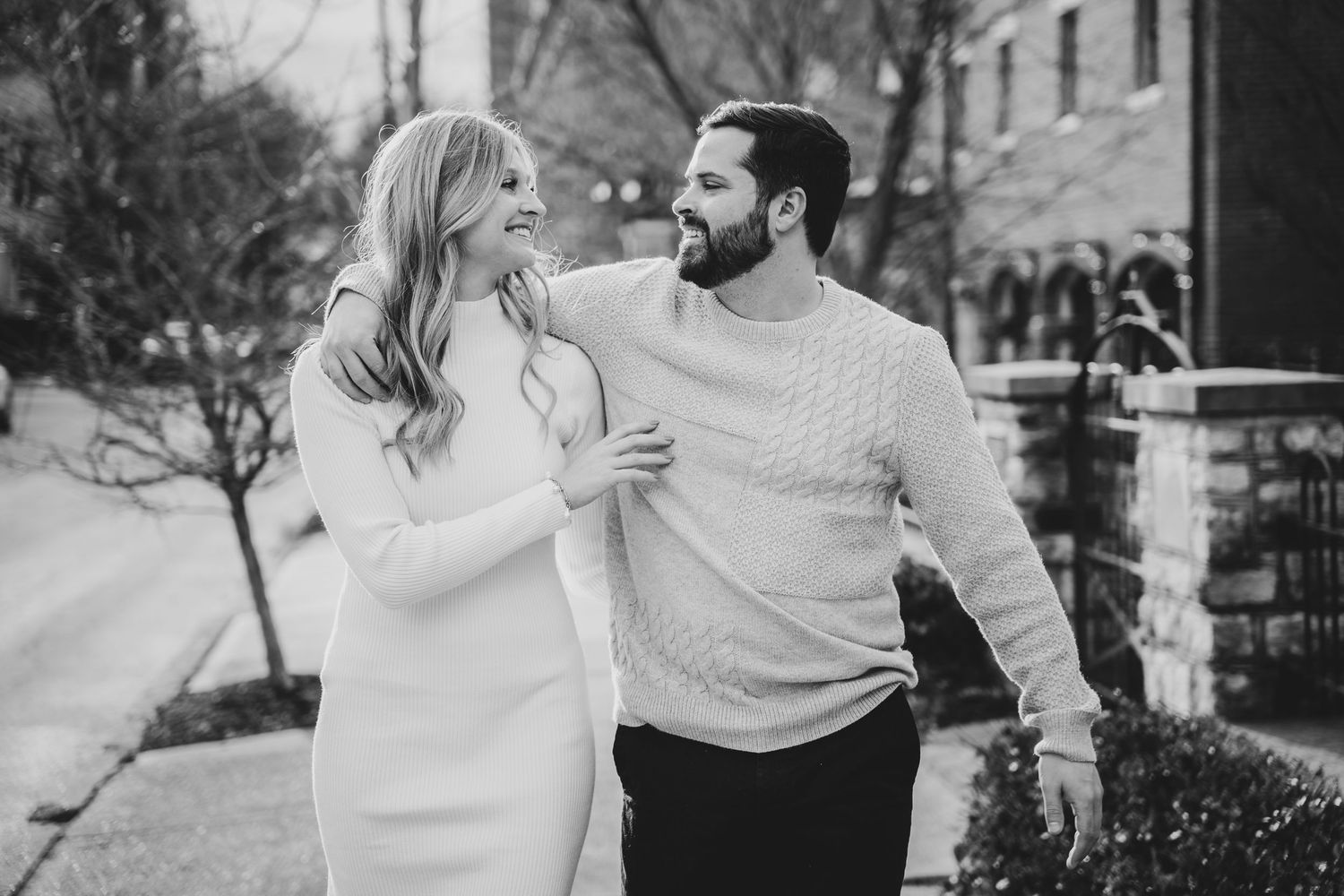 A couple in matching white sweaters shares a loving laugh while walking together in black and white photography.