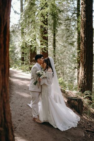 A romantic wedding portrait of a couple embracing on a forest path among majestic redwood trees.