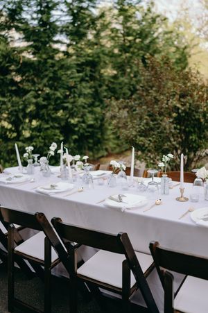 Elegant wedding table setting with white linens, candles and place settings outdoors.