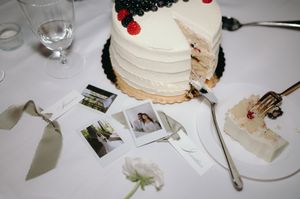 White wedding cake with berries displayed alongside Polaroid photos and table settings.