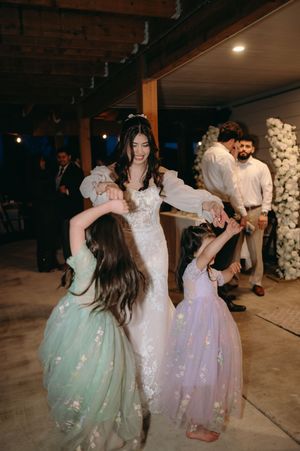 Joyful dancing scene with guests in flowing dresses at an indoor wedding reception.