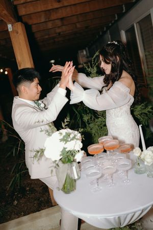 A celebratory moment at a wedding reception with couple high-fiving over a table with champagne glasses.