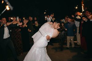A romantic wedding couple shares a dip kiss while dancing surrounded by wedding guests.