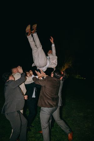 Wedding guests tossing a person in the air during nighttime celebration.