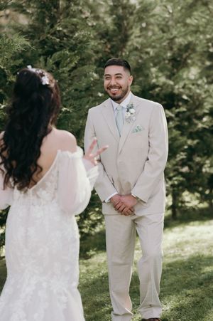 Wedding first look moment captured outdoors with person in beige suit reacting joyfully.