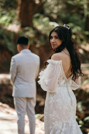 A romantic wedding moment captured in a forest setting with an off-shoulder lace dress.