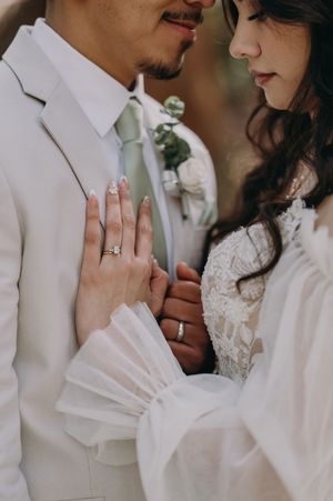 Close-up detail of wedding rings and formal attire showing the couple's hands touching.