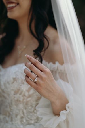 Close-up shot of a bride's hand showing her engagement ring with her lace dress and veil visible.