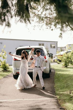 Newlyweds celebrate joyfully while walking away from their getaway car on a sunny day.