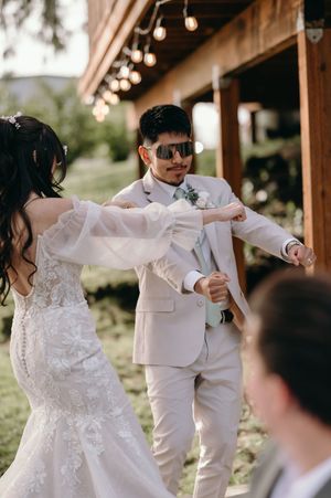 A couple dances during their outdoor wedding reception under string lights and wooden beams.