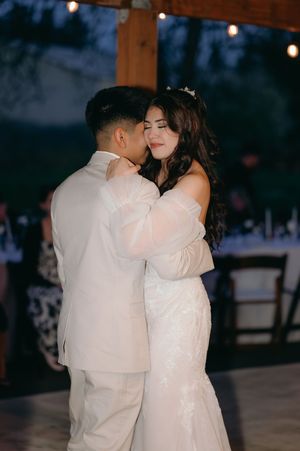 Romantic slow dance between newlyweds under twinkling lights at dusk.