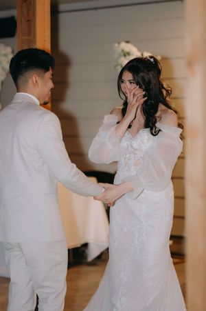 A wedding couple in white attire sharing an intimate first look moment in an indoor venue.