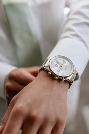 Elegant silver and white chronograph watch on wrist with white sleeve in soft focus background.