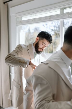 Someone in a light colored suit jacket adjusting clothing near a bright window.