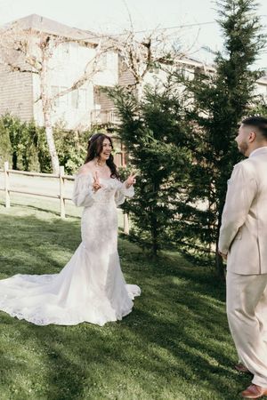 A couple shares their wedding vows outdoors on a sunny day with a white gown and beige suit.