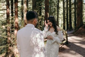 A wedding photography session taking place on a sunlit forest path among tall evergreen trees.