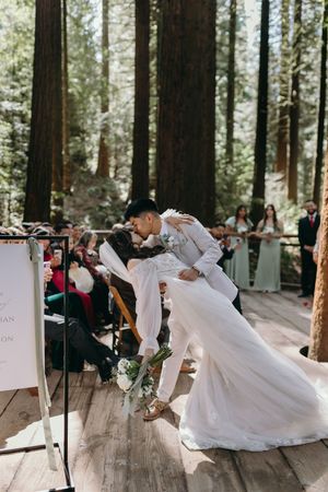 A dramatic wedding kiss during the ceremony on a wooden deck in a forest setting.