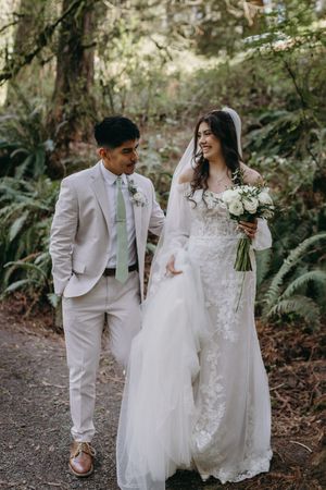 A couple takes a romantic walk through a forest path after their wedding ceremony.