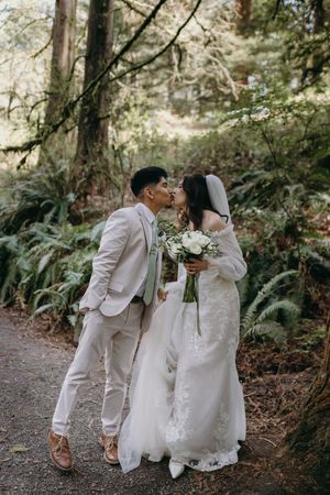 A romantic wedding photo on a forest trail with white floral bouquet.