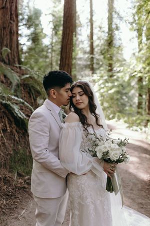 A romantic wedding moment captured in a redwood forest with white floral bouquet.