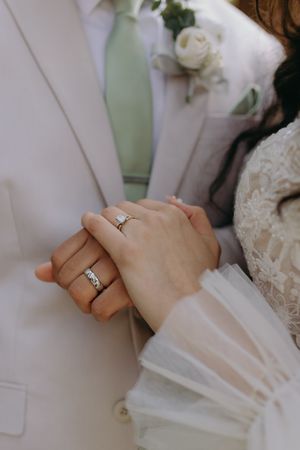 Close-up shot of hands with wedding rings showing white formal attire and a white rose boutonniere.