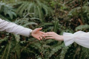 Close-up of hands reaching toward each other against lush green forest foliage.