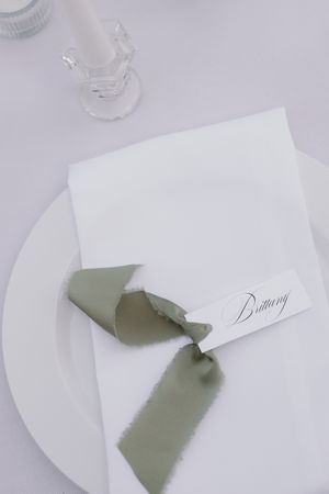 Elegant place setting with white plate and sage green ribbon on white tablecloth.