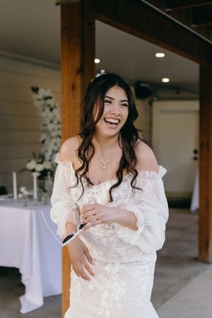 Bride in an off-shoulder lace wedding dress laughs joyfully during wedding celebration.