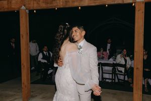 A couple shares their first dance together at a rustic barn wedding reception under wooden beams.