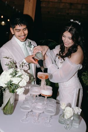 A couple pours champagne into a tower of glasses at their wedding reception.