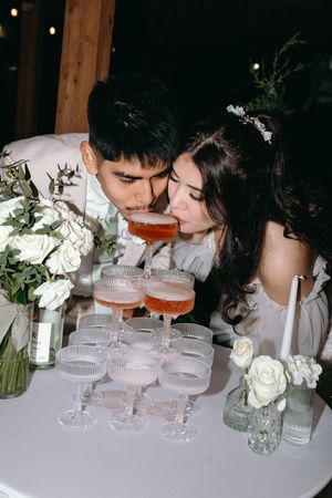 Couple sharing cocktails at wedding reception with white roses and elegant glassware.