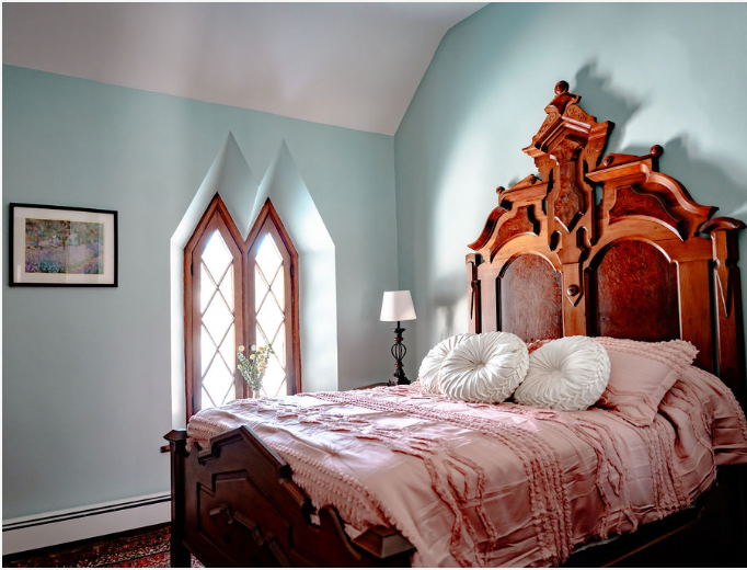 Gothic bedroom features ornate wooden headboard, pale mint walls, and pointed arch diamond-pane windows with pink bedding.