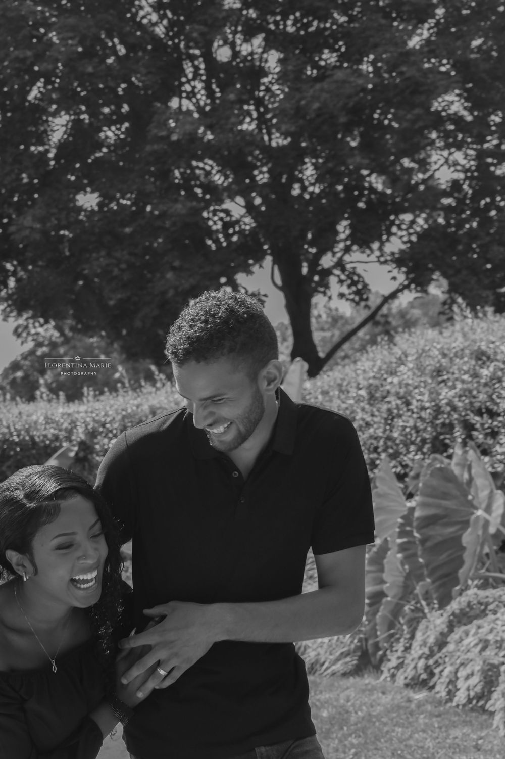 A joyful couple sharing genuine laughter against a backdrop of trees and sunlit foliage.