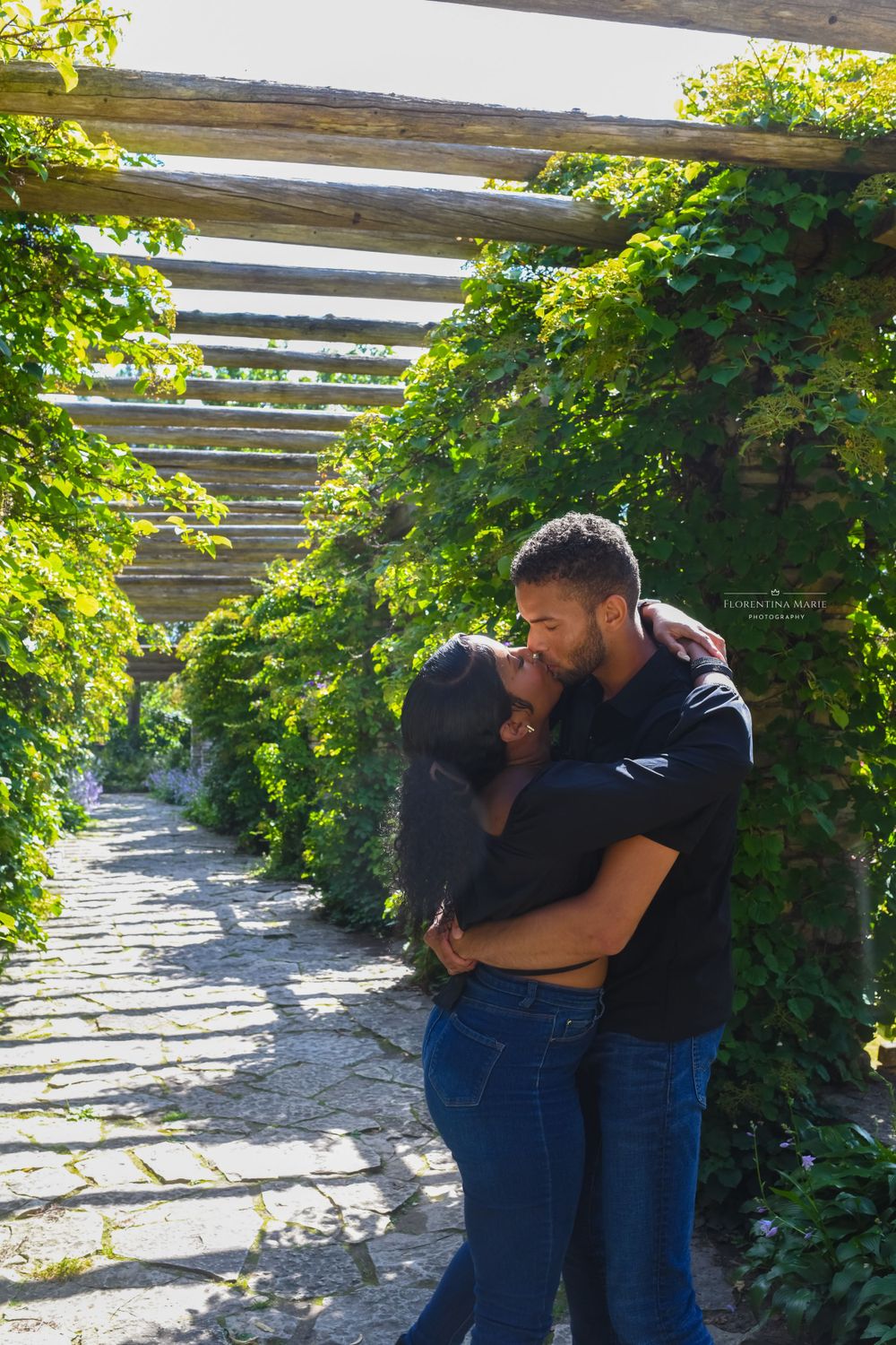 Loving couple sharing an intimate embrace under a vine-covered garden pergola.