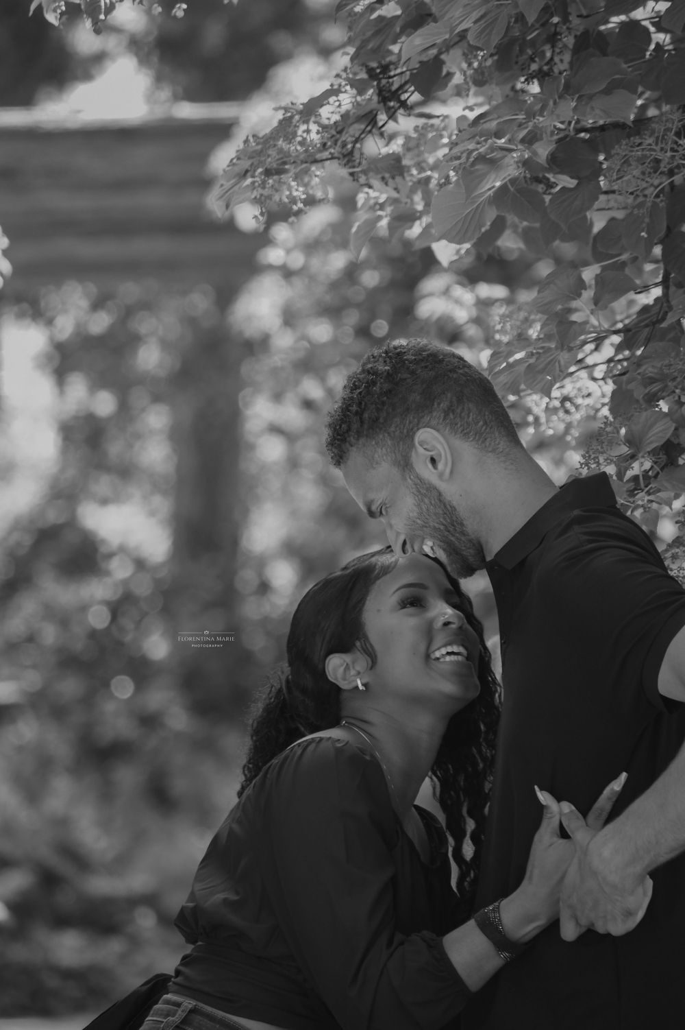 Black and white photo capturing a couple's laughter and embrace among garden foliage.