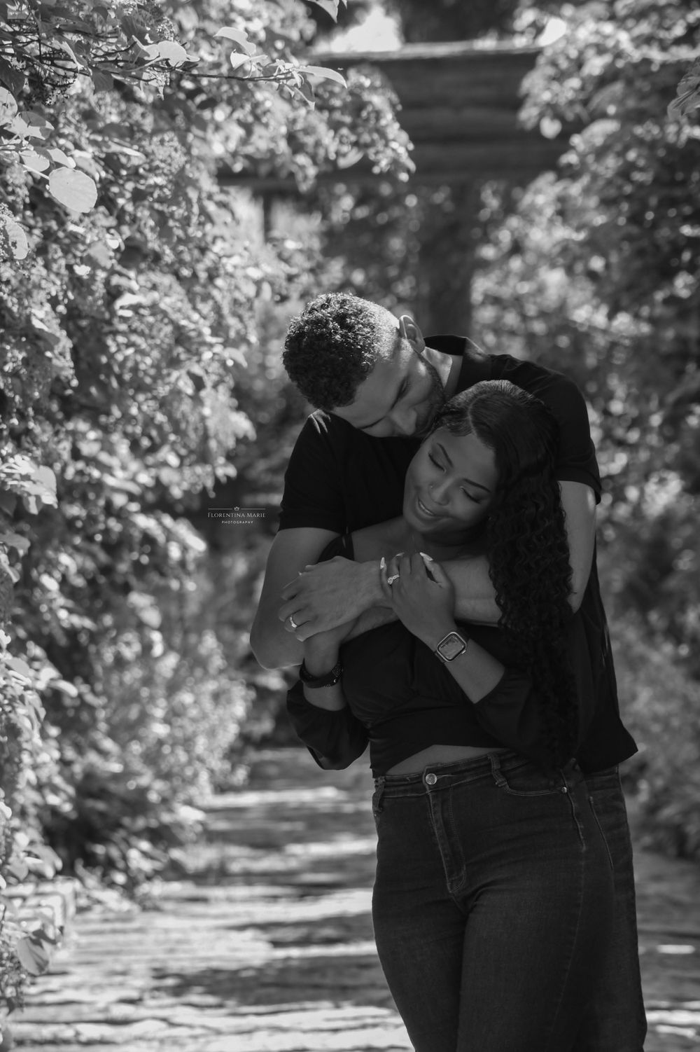 A tender embrace between a couple surrounded by lush foliage in a garden setting.