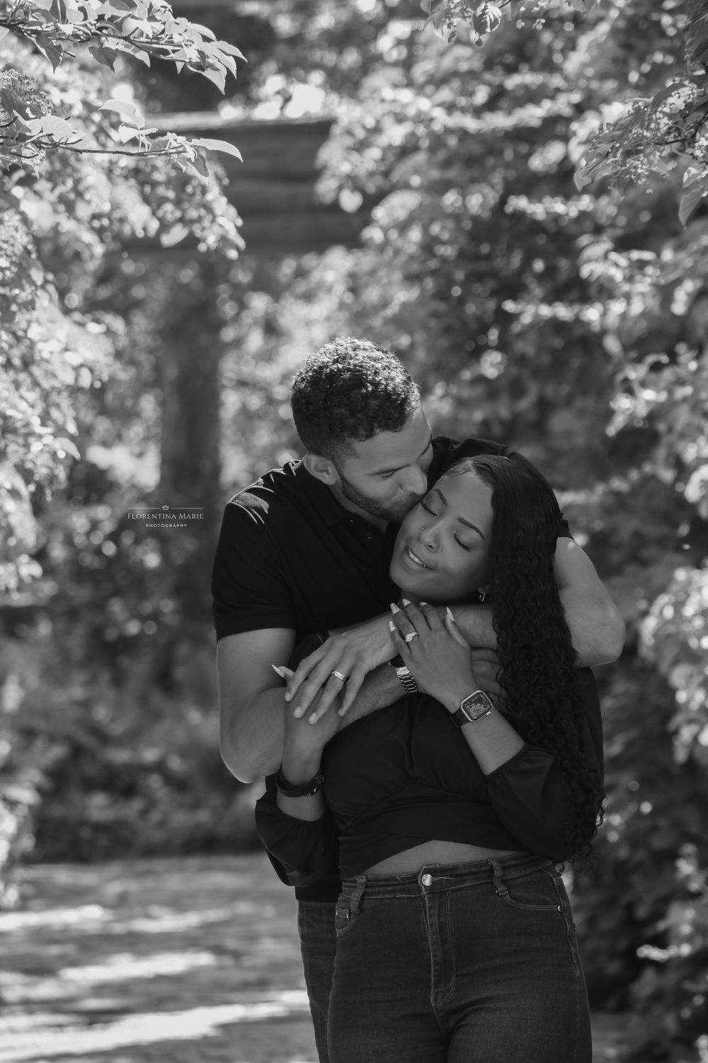 An intimate black and white portrait of a couple sharing an emotional moment in a garden pathway.
