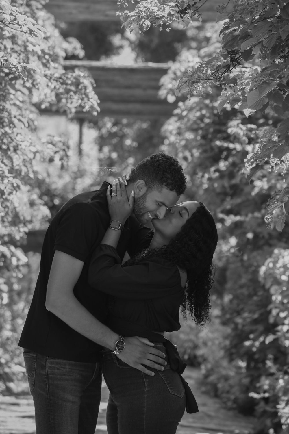 A loving couple shares a romantic kiss on a garden path framed by blooming trees.
