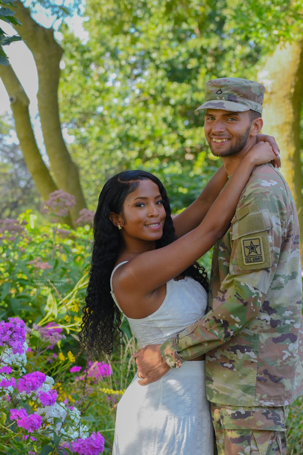 A joyful outdoor portrait of a couple embracing in a garden with purple flowers.