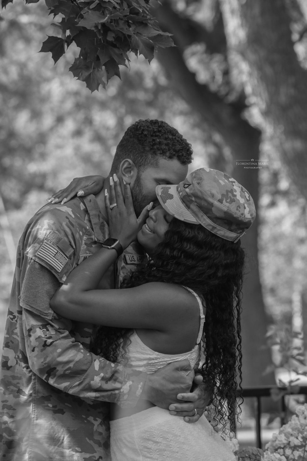 A romantic black and white moment between a service member in uniform and partner under leafy trees.
