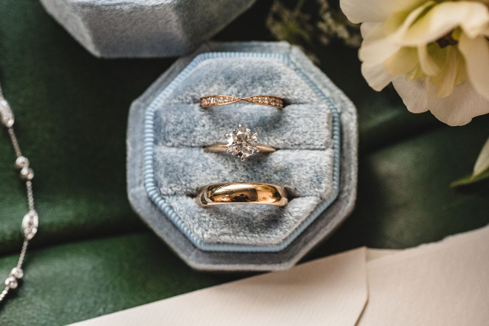 Close-up of engagement and wedding rings displayed on gray textured surface with white flowers.