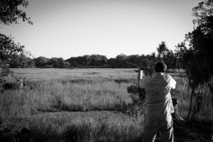 Person photographing scenic grassland landscape in black and white.
