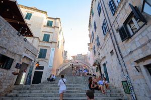 Historic stone stairway in Mediterranean old town with tourists exploring ancient architecture.