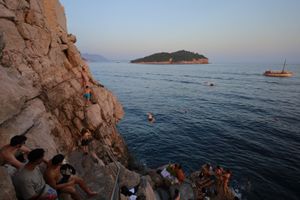 Cliff jumping spot overlooking blue Adriatic Sea with small island in distance.